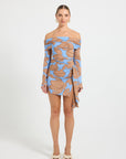 Woman wearing a blue and brown floral printed off-shoulder dress with asymmetrical tie detail at the hip.