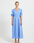 Woman wearing a light blue V-neckline button-through midi dress with elbow-length puffed sleeves.
