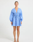 Woman wearing a light blue linen V-neckline long-sleeve mini dress.