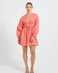 Woman wearing a coral linen V-neckline long-sleeve mini dress.