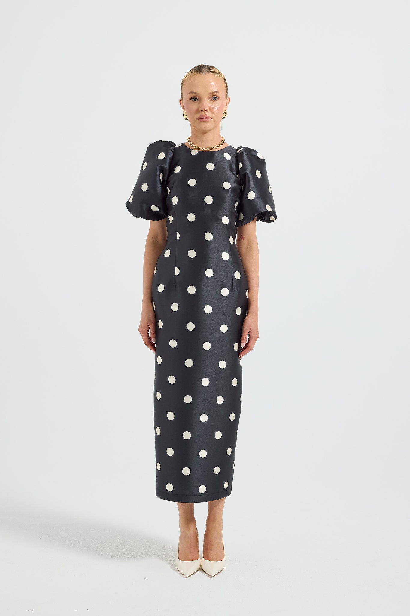 Model wearing a black and white polka dot high neck fitted midi dress with short puff sleeves