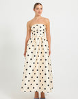 Woman wearing a strapless cream and black polka dot flared midi dress.