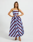 A woman modeling a strapless maxi dress with a chevron stripe in light blue and burgundy, standing against a light studio background.