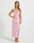 A woman modeling a sleeveless midi dress with a pink and light blue floral pattern, standing against a plain light gray studio background.