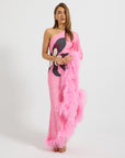 A woman models a one-shoulder pink gown with a black and white graphic print on the bodice and a fluffy pink feather boa draped over one arm, set against a plain light gray studio background.
