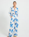 Woman wearing white and blue floral print high-waisted wide-leg pants on a white background, paired with a matching long-sleeve shirt.