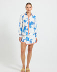 Woman wearing a white long sleeve button through shirt with blue floral pattern and matching skirt on a white background.