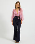 A woman modeling a pink floral long-sleeve tie-front blouse and dark navy flared jeans against a plain light gray studio background.