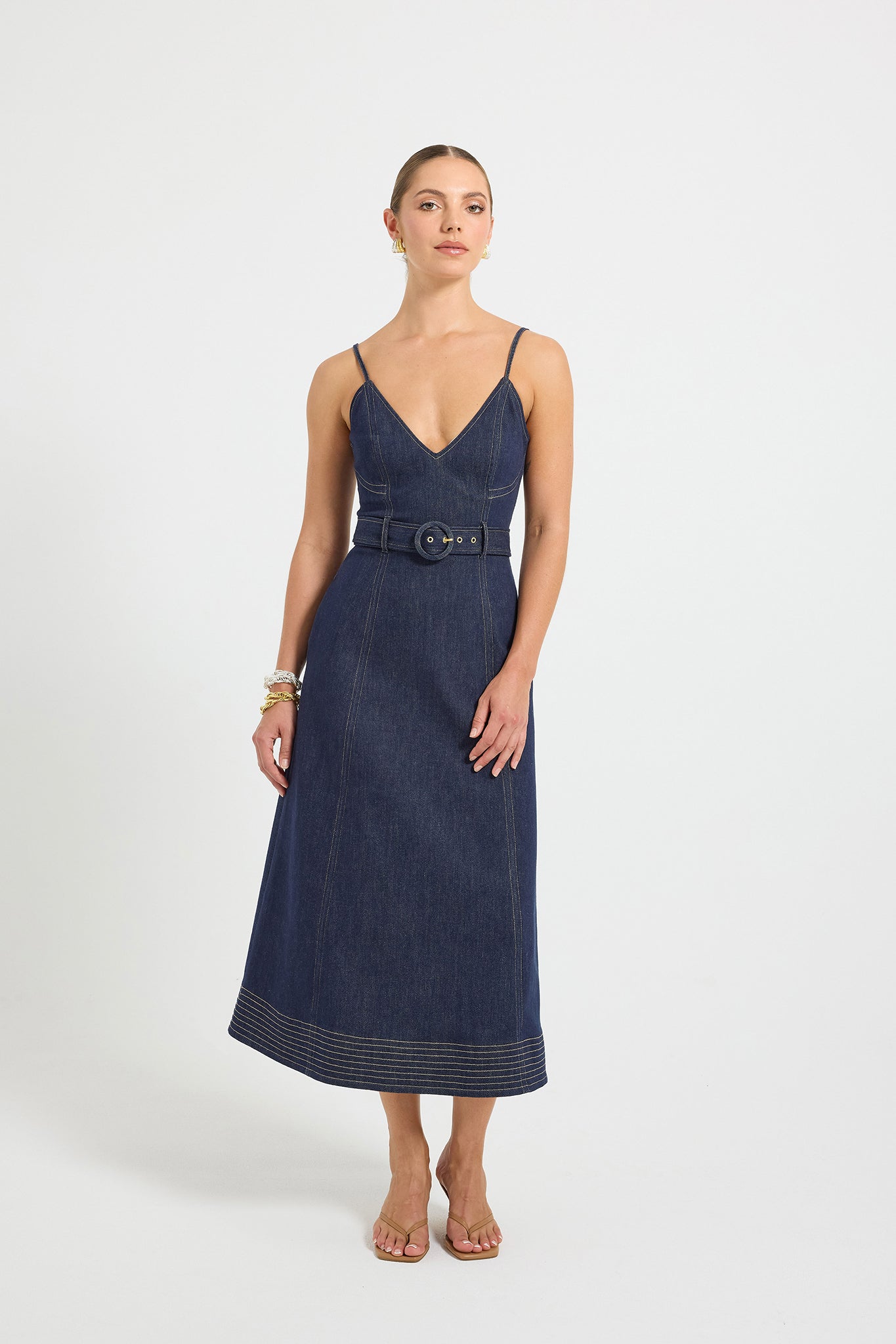 Woman wearing an indigo denim dress with a V-neckline, contrast topstitching, and a belt on a white background.