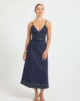 Woman wearing an indigo denim dress with a V-neckline, contrast topstitching, and a belt on a white background.