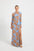 Woman wearing a long blue and brown floral dress with a high boat neckline.