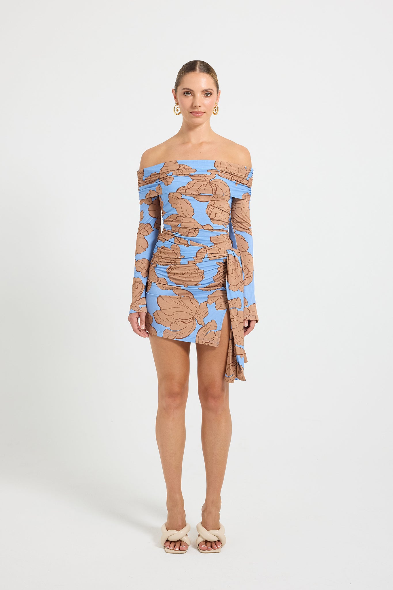 Woman wearing a blue and brown floral printed off-shoulder dress with asymmetrical tie detail at the hip.