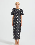 Model wearing a black and white polka dot high neck fitted midi dress with short puff sleeves