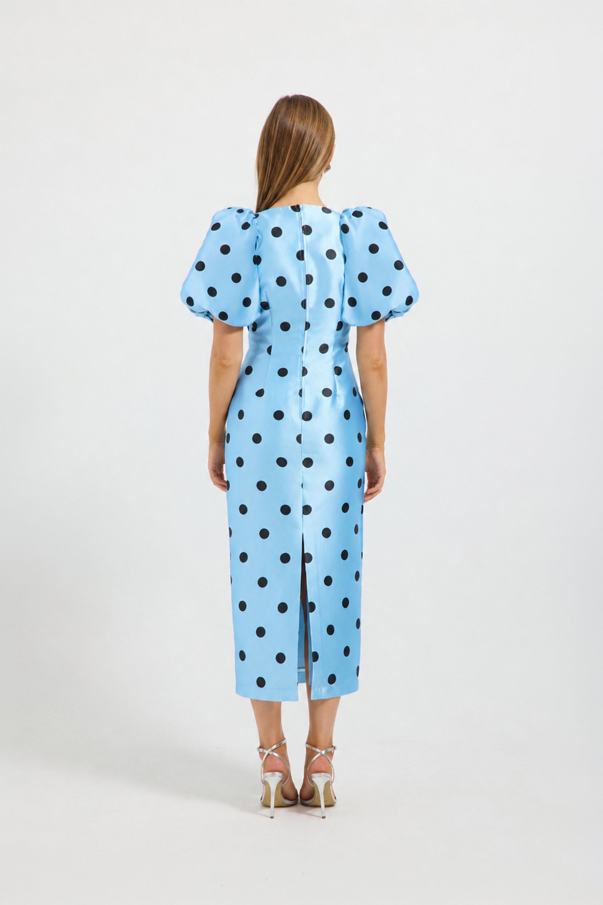 A woman viewed from the back wearing a light blue midi dress with black polka dots and puffed short sleeves. 