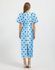 A woman viewed from the back wearing a light blue midi dress with black polka dots and puffed short sleeves. 