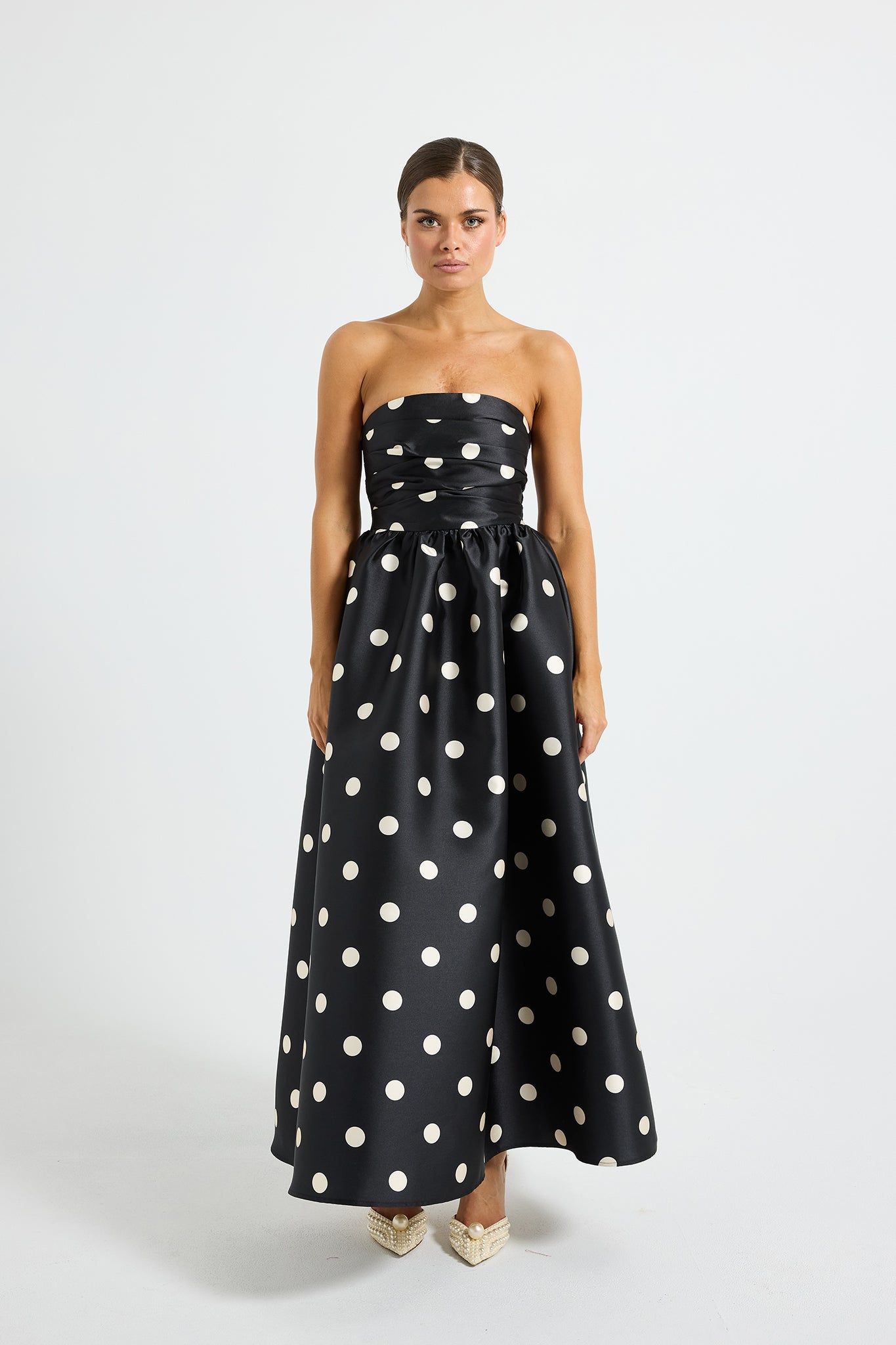 Woman wearing a black strapless midi dress with white polka dots 
