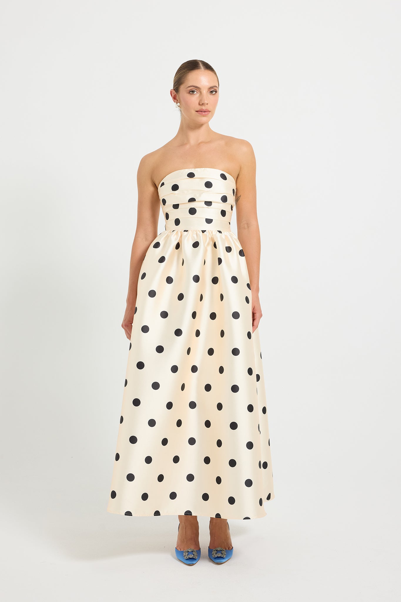 Woman wearing a strapless cream and black polka dot flared midi dress.