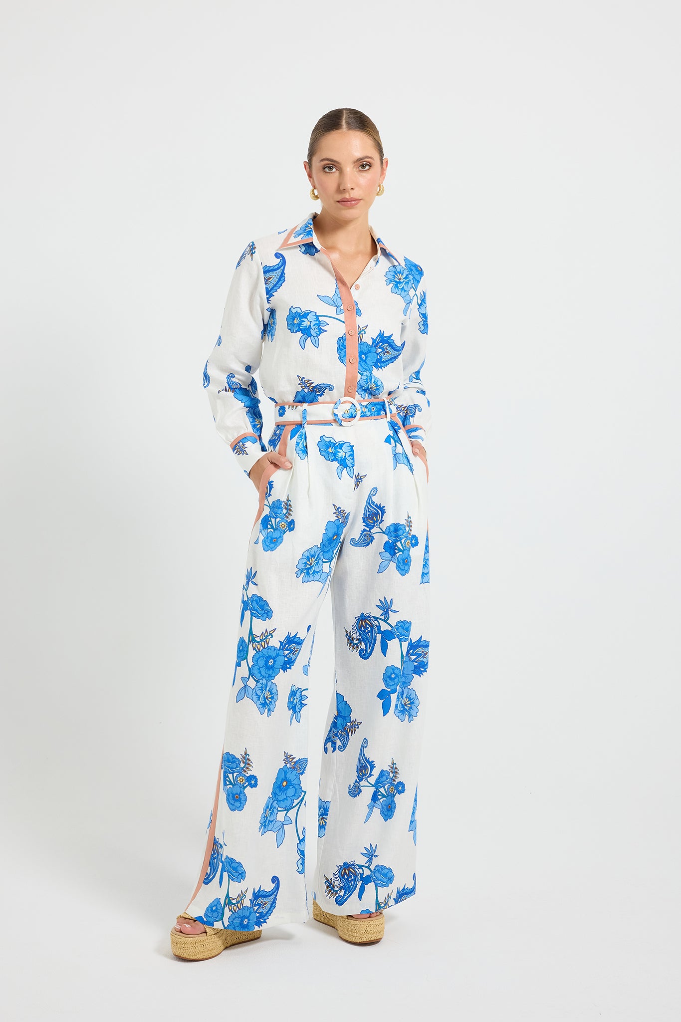 Woman wearing white and blue floral print high-waisted wide-leg pants on a white background, paired with a matching long-sleeve shirt.